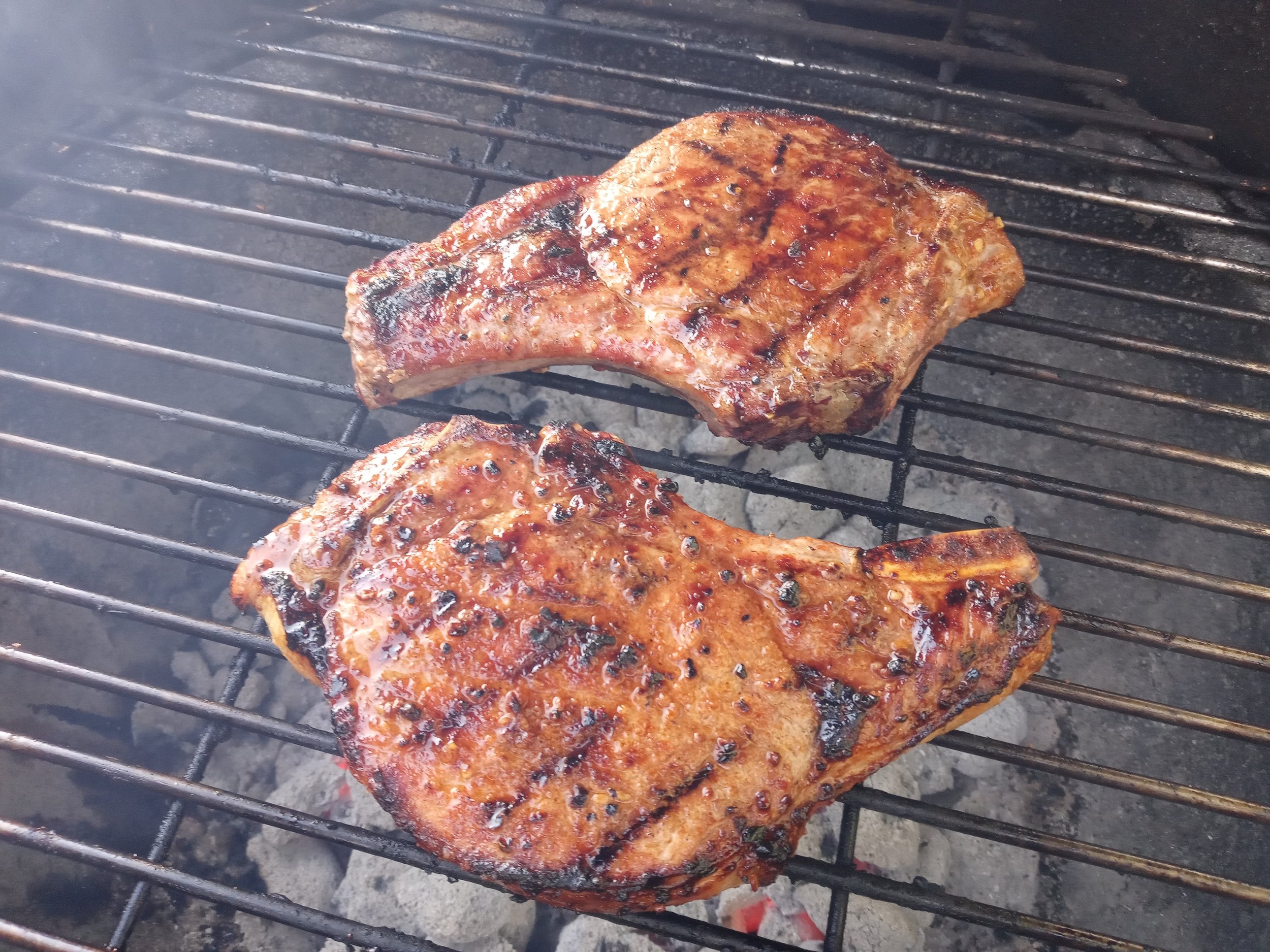 Grilled pork chops sizzling on a barbecue grill, showcasing a rich brown glaze and grill marks, surrounded by smoky ambiance.