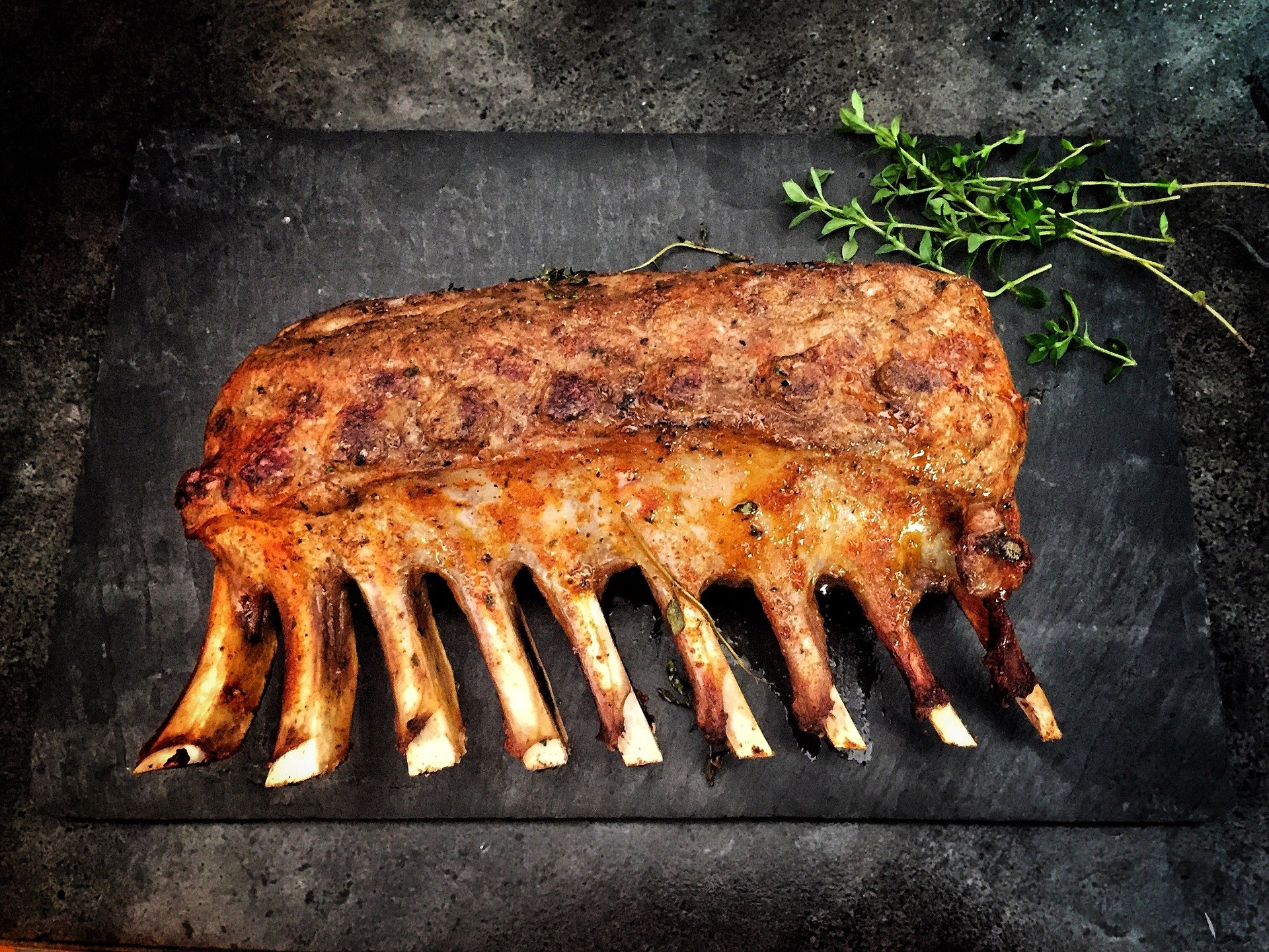 Roasted rack of lamb on a dark slate board, garnished with fresh thyme, showcasing its golden-brown crust and tender meat. Perfect for gourmet dining and special occasions.